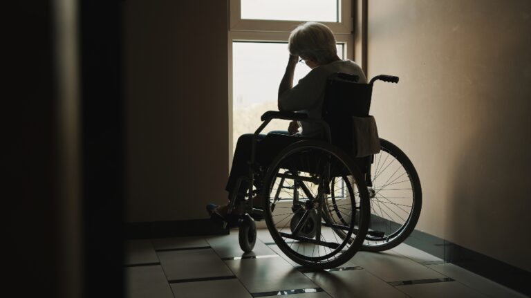 lonely senior woman looking through the window of the nursing home