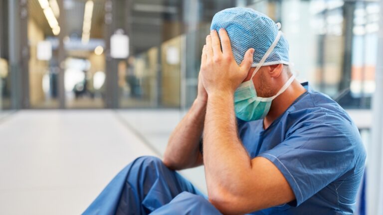 Desperate surgeon in blue surgical clothes with hands in front of the face