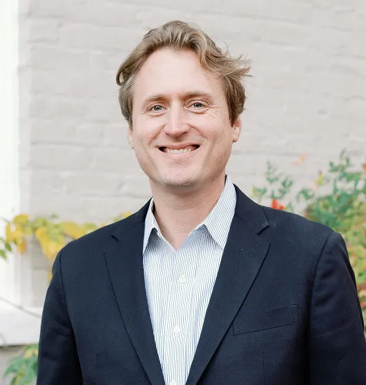 Professional portrait of a smiling man in a dark blazer and striped shirt.