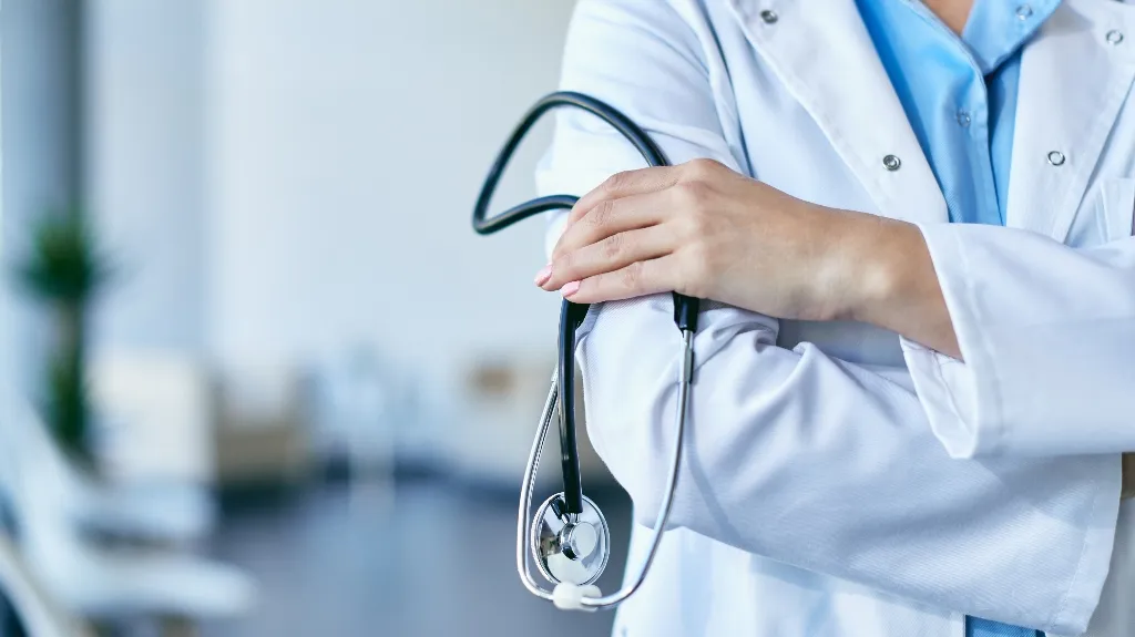 Healthcare professional in white coat holding a stethoscope with arms crossed.