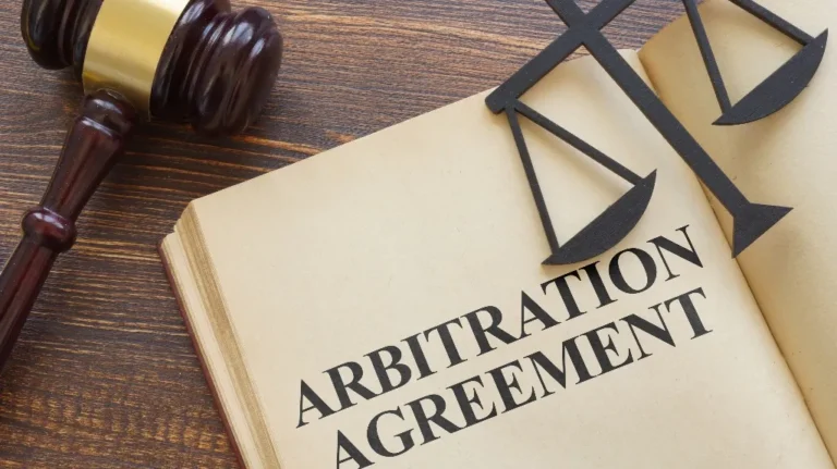 Open book displaying the text "Arbitration Agreement" with a wooden gavel and scales of justice.