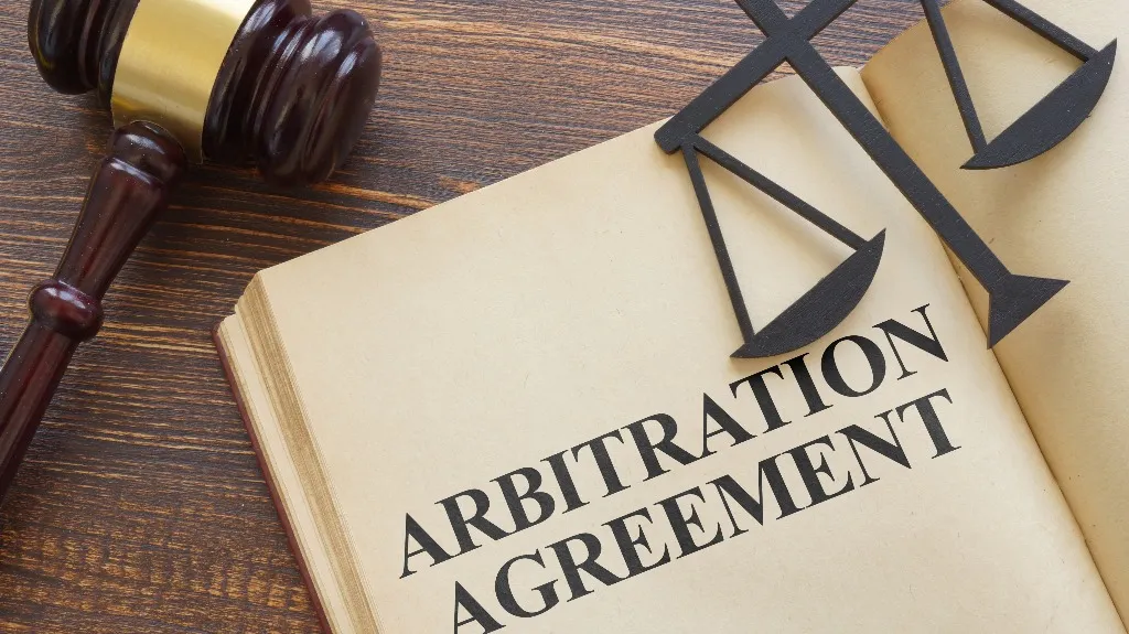 Open book displaying the text "Arbitration Agreement" with a wooden gavel and scales of justice.
