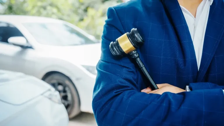 Person in blue suit holding a black and gold judge's gavel with white cars in background.