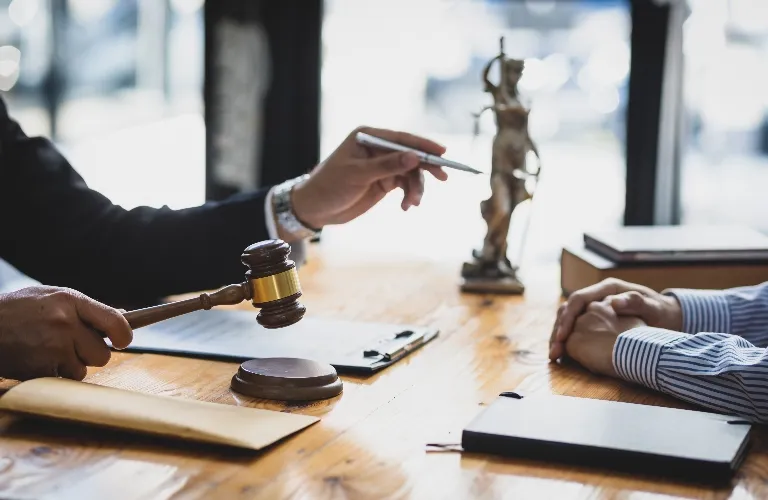 Two people at a wooden table with a judge’s gavel, legal documents, and Lady Justice statue.