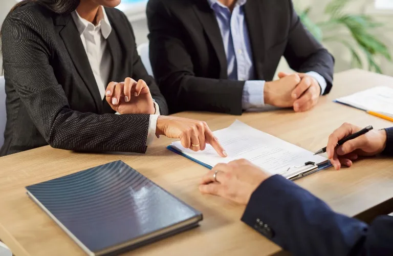 Three professionals in business attire reviewing and discussing a document at a wooden table.