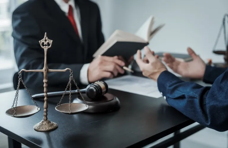 Two professionals in discussion at a desk with a balance scale and gavel present.