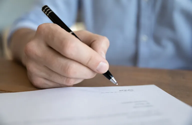 Close-up of a person holding a black pen, poised to sign a document on a wooden table.